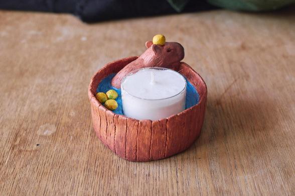 The same candle holder seen from the back. Three yuzu fruits are floating and one is perched atop the capybara's head